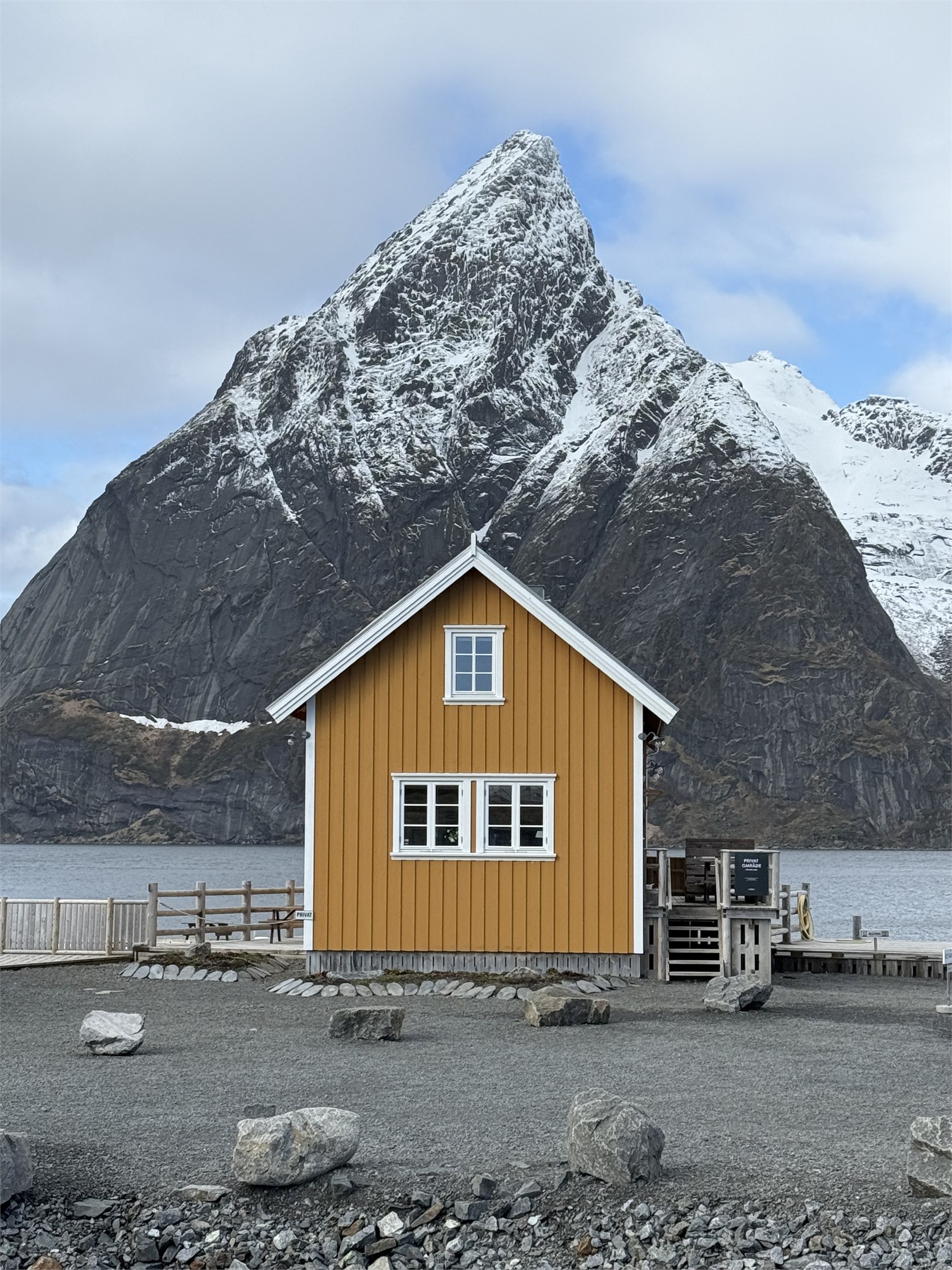 Yellow cabin below a snow-covered mountain in Lofoten
